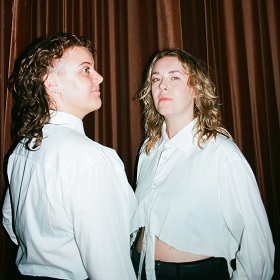 Photo of Emma Kew and Cherryn Frost, both aetists pose for the camera and stand infront of a brown stage curtain