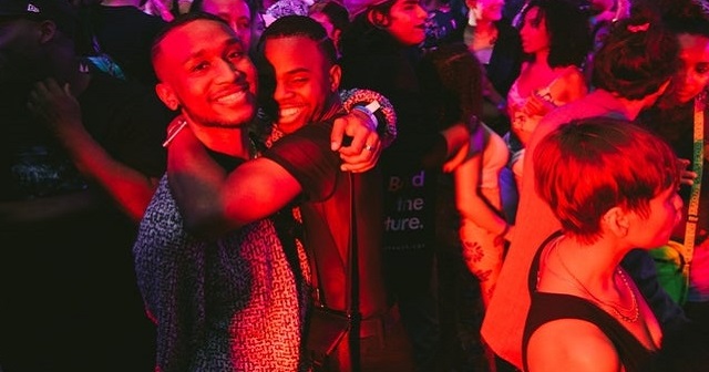 Photo of happy people in crowd, red lens, two men happily embrace each other at centre of photo and crowd