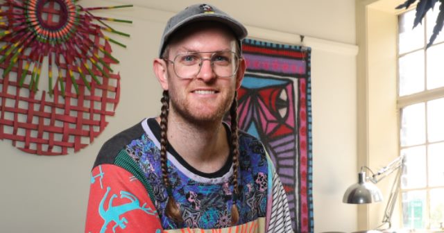 Artist Jeff McCann photograph, colour, wearing cap, pigtails, wearing colourful patterned  t-shirt 