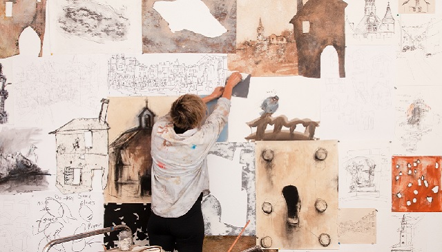 Photo of Jody working on a large artwork, there looks like mixed media, drawing, water colour, illustration