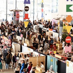 A busy market photo showcasing many stalls with arts and crafts, crowds of people