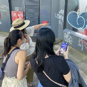 Photo of three people on the hunt pointing at a mural on a wall and using phone to scan