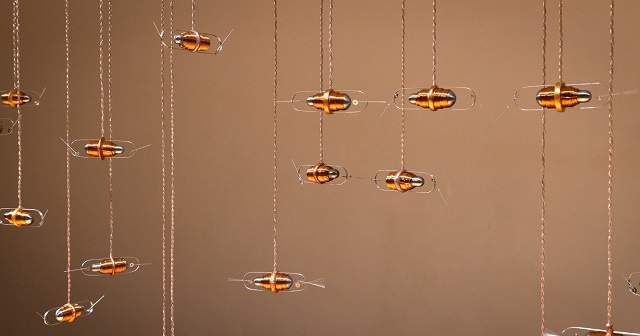 Tom Kind, Push/Pull at Chrissie Cotter Gallery May 2021, hanging bronze sculptural artwork , vertical paper clip shaped silver holds bullet type shape bronze centred piece with another centre reinforcing bronze tone cylindrical clasp