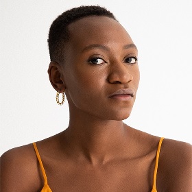 Portrait photo of playwright black woman Moreblessing Maturure, Moreblessing looks at camera she has short cropped hair, orange spaghetti straps and a gold earring, 