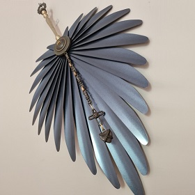 Photo of a sculptural work, the piece looks like a large silver leaf with defined concertina type ridges, down the centre of the piece there is an ornate strip which turns into what looks like a handle at the top the materials look like metal beads and decorative ornaments