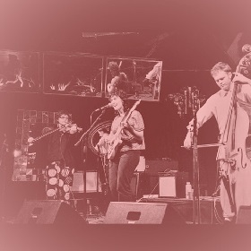 Purple filter over photograph of band playing on stage, violinist, cellist and guitar plater/singer