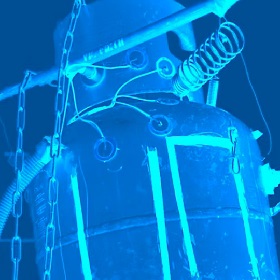 A blue tone photograph which has an illuminated filter on the photo - the photo is of a gas bottle that has a number o items added to it like a spring, chains and wire