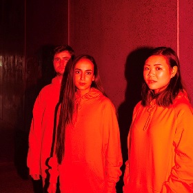 Black and white photograph of three performers head and waist  wearing hoodies red lens
