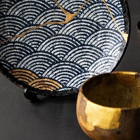 Photo of plate with Japanese art of kintsugi applies whereby liquid type gold substance is applied to stick together broken ceramics. Japanese style black pate with white lines and gold fluid shape biding cracked ceramic plate together