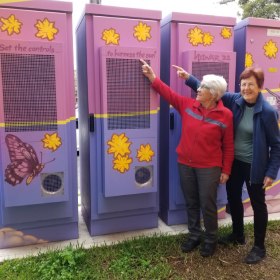 Two women pointing at large community battery units