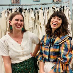 Two smiling women standing in front of racks of clothes