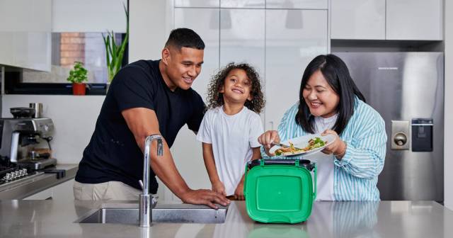 man, child and woman in kitchen scraping scraps into food caddy
