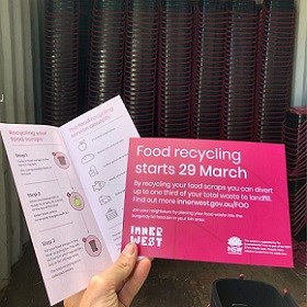 Hand holding two flyers, one pink says Food recycling starts 29 March