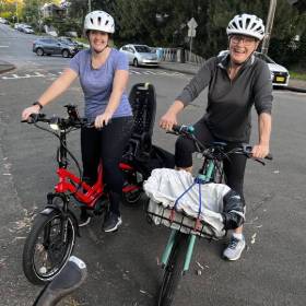 Two women on bikes smiling at the camera stopped on a suburban street