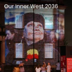 Photo of an Indigenous woman projected onto a brick building at night with people standing in front of it.
