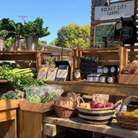 Wooden boxes and hand woven baskets arranged on shelves outside filled with fresh vegetables and jams