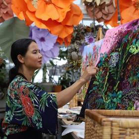 Woman painting with lots of flowers around her and on her clothes 