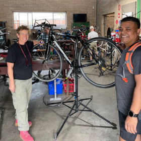 Two people standing by a propped-up bike in a maintenance workshop.
