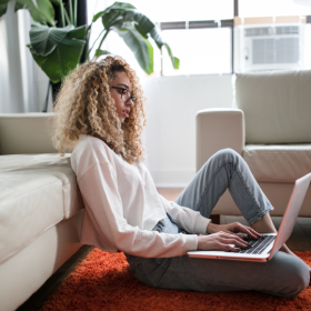 woman sitting on floor leaning up against couch holding laptop