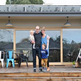 Man, woman and two children standing on the back porch of their home with solar panels in view on roof