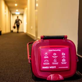 Maroon lidded bucket on floor of corridor with person disppearing in the distance