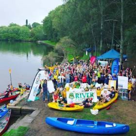 Group of people standing on river edge with kayaks