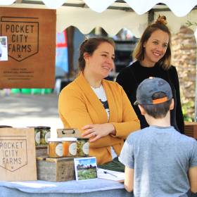 Two women at market stall speaking with customer