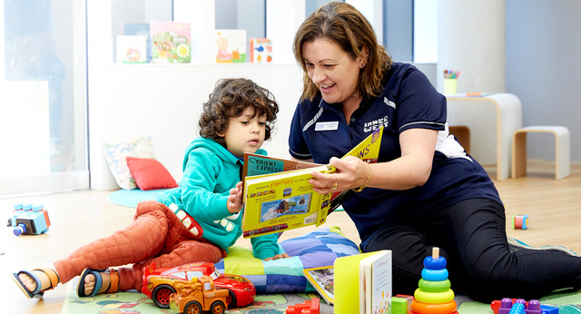 Woman sitting on the floor with child reading a book surrounded by toys