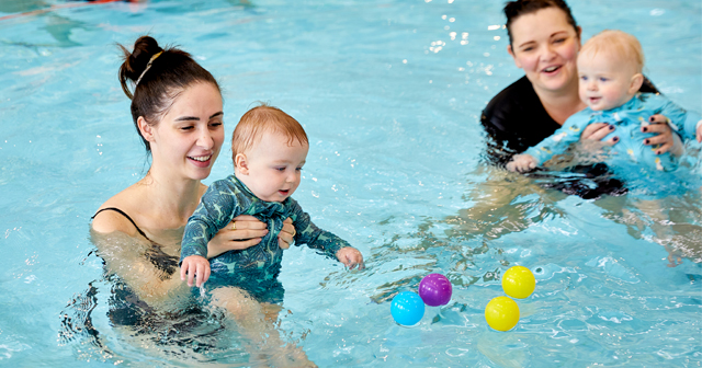 Parent holding up baby playing with colourful balls floating in the water