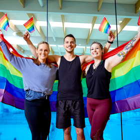 Three people holding up rainbow pride flags and smiling