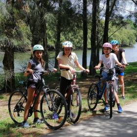Four young people with bikes standing in front of a river and trees