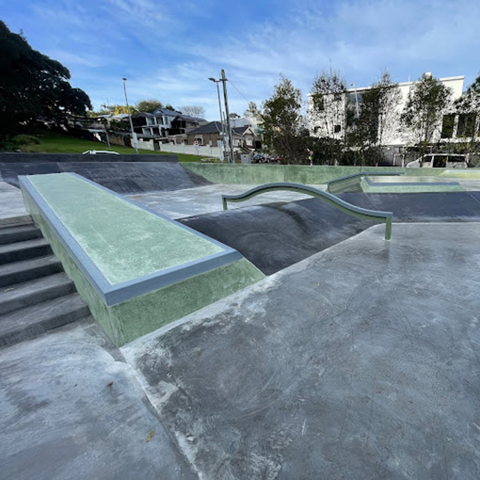 A modern skate park with a lawn and various houses in the background