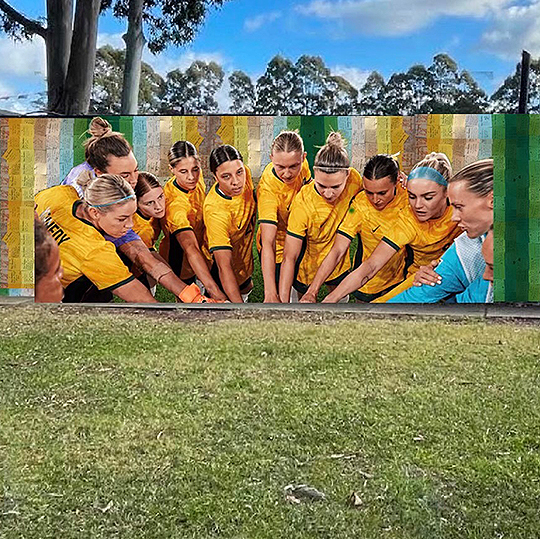 Painting of players from the Australian women's football team, holding our their hands at a central point for a team huddle