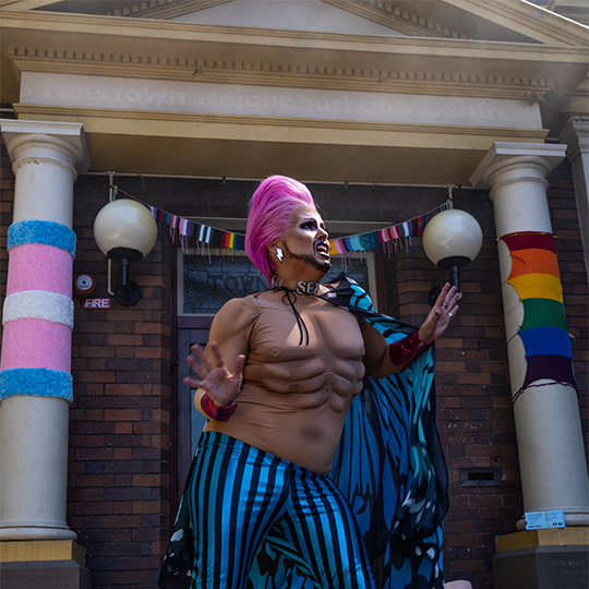 drag king performing in a pink wig in front of a Town Hall building