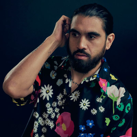 headshot of Omar Musa in a flowered patterned shirt running one hand through his hair