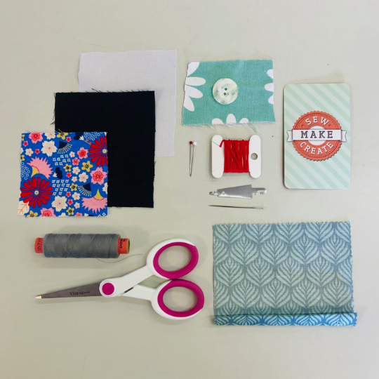 small pieces of coloured squares of fabric laid out on a table with sewing scissors, cotton and pins.