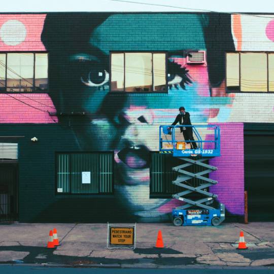 artist Brad Robson in a cherry picker painting an image of Twiggy onto a building