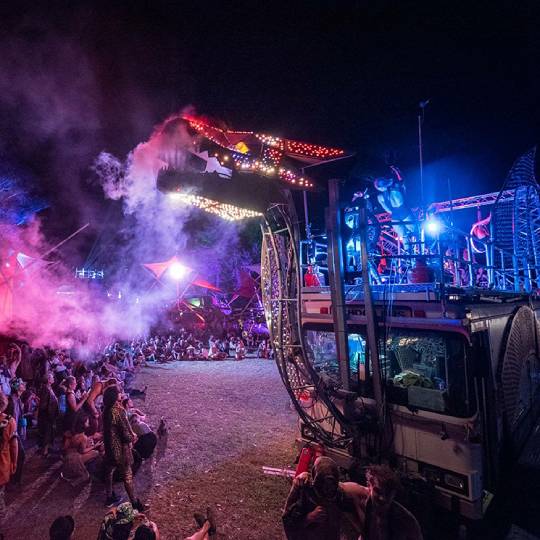 a crowd watches a smoke breathing dragon made from industrial waste