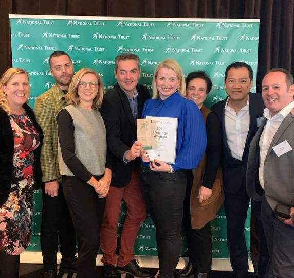 council staff and architects holding an award in front of a sign for the National Trust