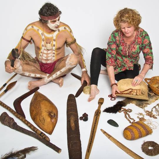 a man and woman sit in a white room surrounded by Aboriginal artefacts