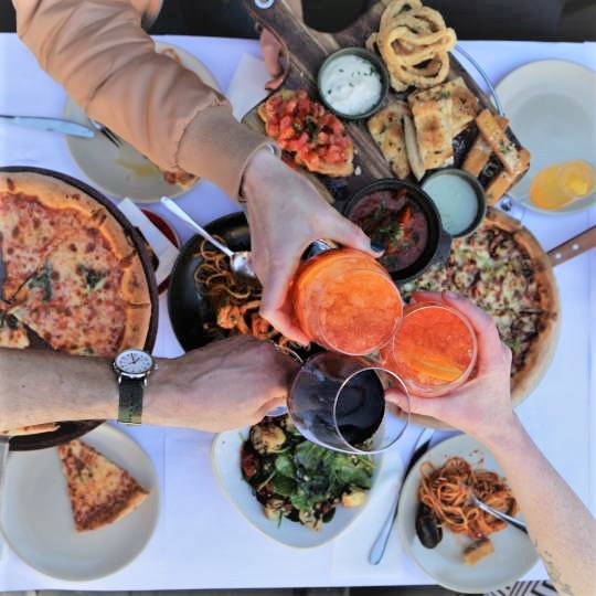 hands holding drinks above platters of food on a table