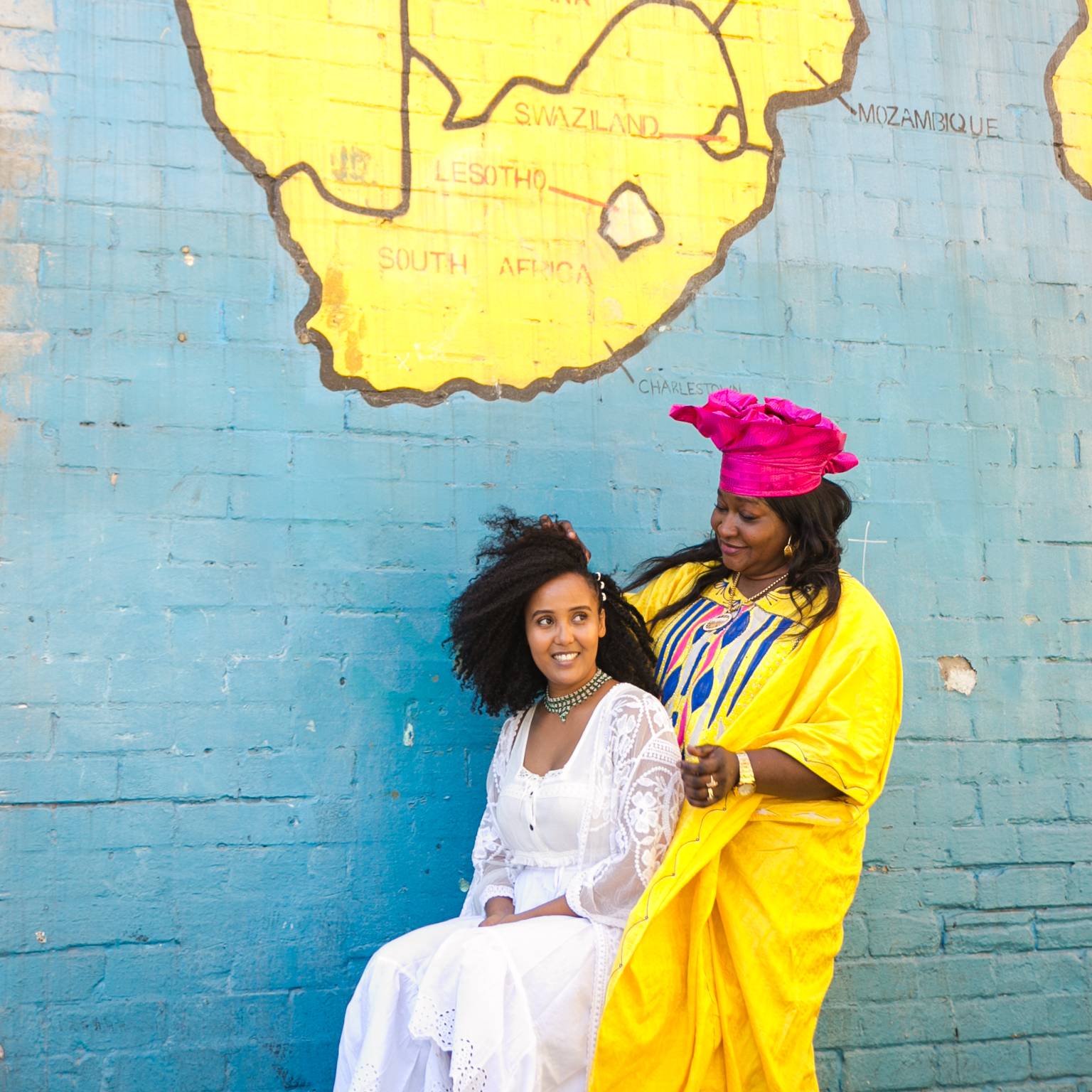 two women standing in front of a wall while one woman has her hair braided