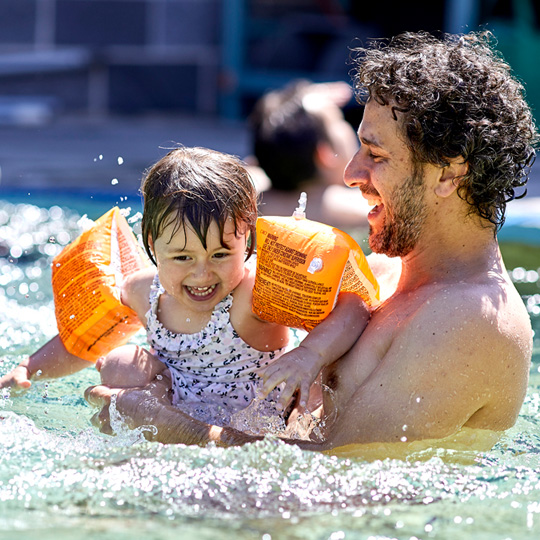 Man and baby wearing orange floaties in a pool