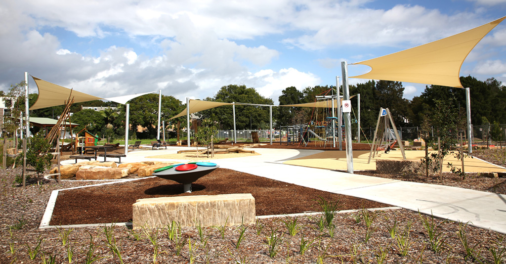 A shaded playground area with young landscaped plants and mulch around it.