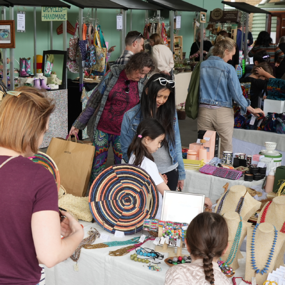 poeple browsing jewellery and handicrafts laid out on tables at an indoor market