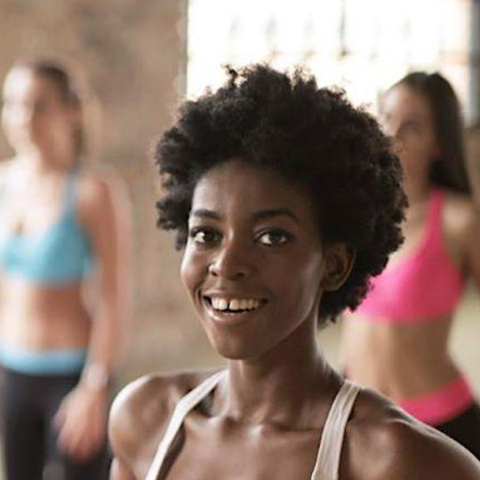 Smiling woman at a dance class to children in coloured spandex are in the background