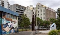 Large red brick and cream historic building with Mungo Scott Ltd Flour Millers on the side next to newer grey residential buildings plus graffitied small building in foreground