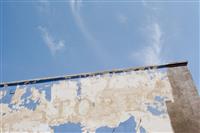 Blue palleted image with an old building wall with peeling blue paint and the word Stores against a blue sky with slight wispy clouds