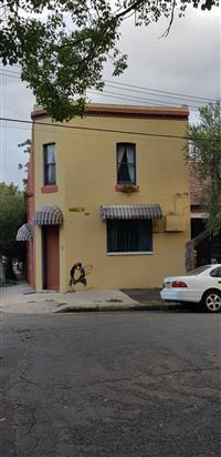 Small yellow building with orange accents striped window covers and monkey graffiti plus white car road and natural framing