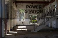 Darkened run down space with white and white washed brick walls staircase leading to right of the image and the words Power Station set onto the wall